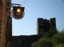 Monteriggioni (SI) - Particolare delle mura difensive con la sommita di una torre. Sulla sinistra un antico lampione e la caratteristica insegna di una bottega del vino. In uesta zona viene prodotto il pregiato Chianti dei Colli senesi del Consorzio del Gallo Nero - Fotografia 20 agosto 2011, Toscana